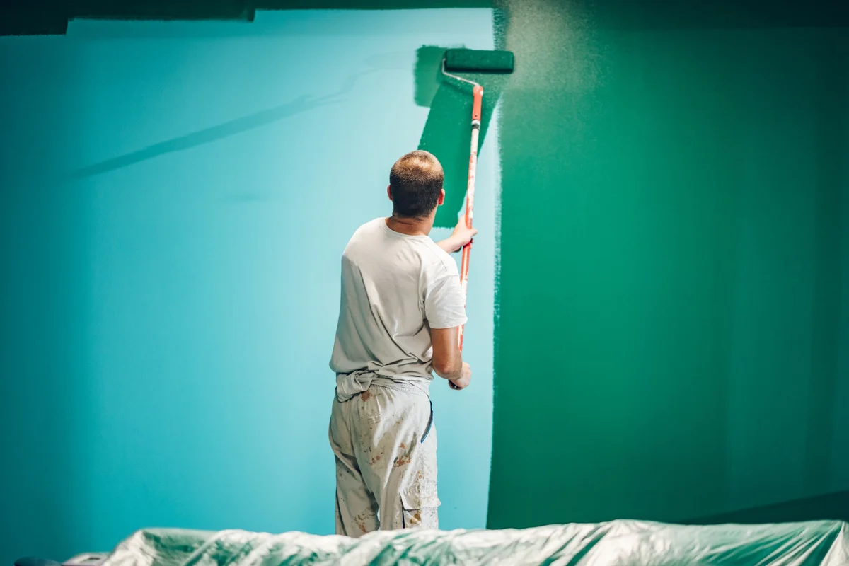 Painter applying paint on a wall, seen from behind during home renovation
