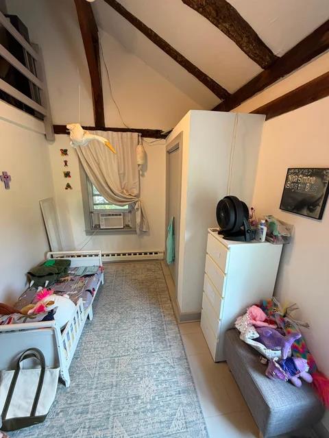 Bedroom interior with exposed wooden beams, white wardrobe, single bed with pink items, dresser, and window with air conditioning unit